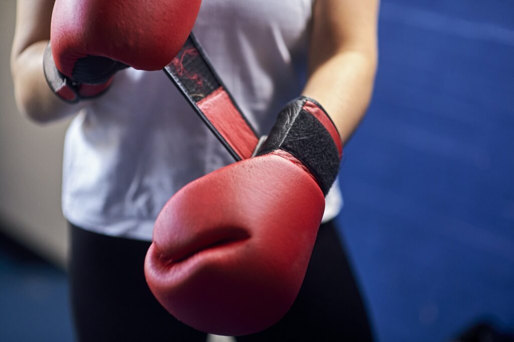 Mid section of female boxer fastening red boxing gloves